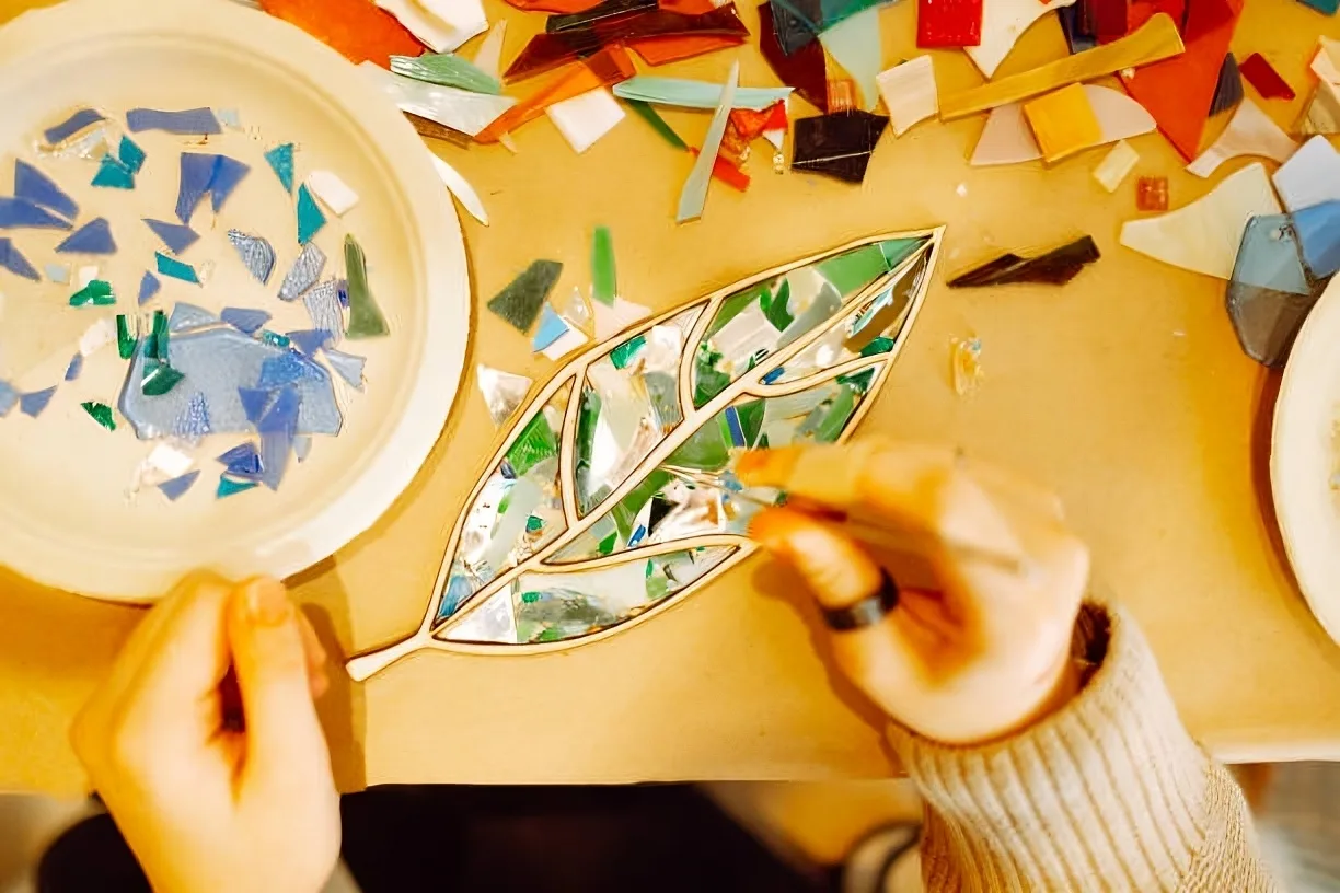 Mosaic artwork – Hands arranging colorful glass pieces to create a leaf design.